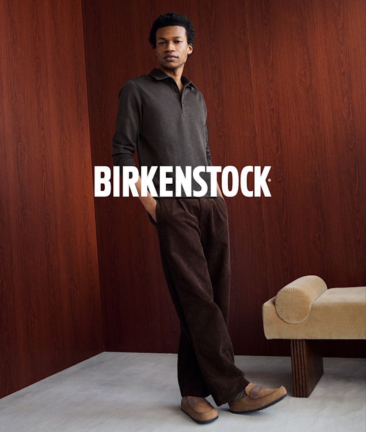 Mann i brune kordfløyelsbukser og grå polo iført beige Birkenstock-loafers i mokkasin-stil.