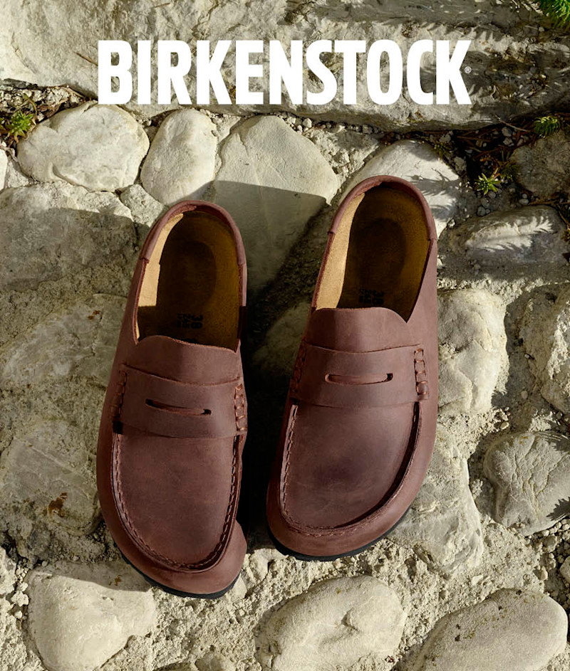 Brune Birkenstock loafers i skinn plassert på steingrunn med BIRKENSTOCK-logo øverst i bildet.