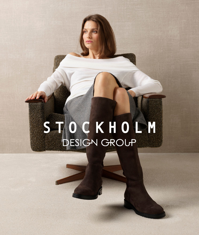 Dame i lenestol med mørkebrune høye støvletter i semsket skinn fra Stockholm Design Group. Kledd i hvit genser og grått skjørt