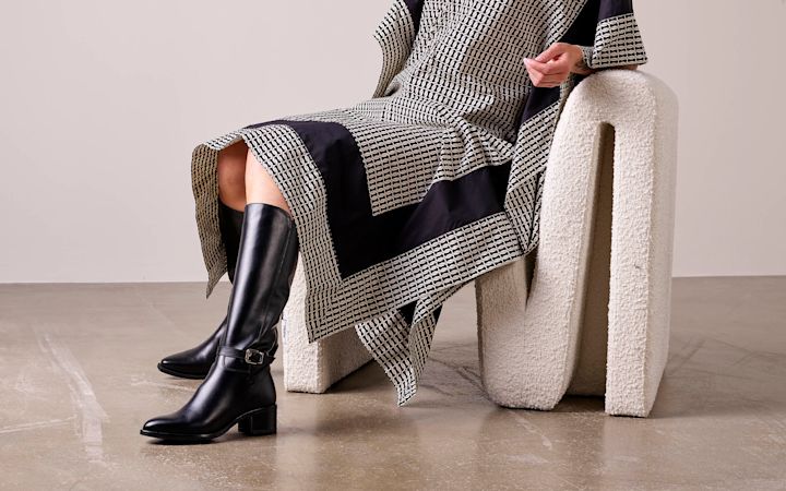 høye sorte støvletter med spenne på fot. modellen sitter i en designerstol