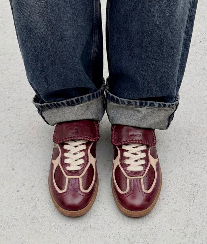 Mørkerøde retro sneakers med beige detaljer og gummisåle, sett ovenfra med oppbrette blå jeans.