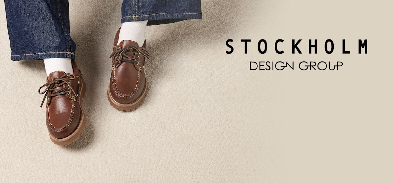 Brune seilersko i skinn fra Stockholm Design Group, vist på en person med jeans og hvite sokker mot en beige bakgrunn.