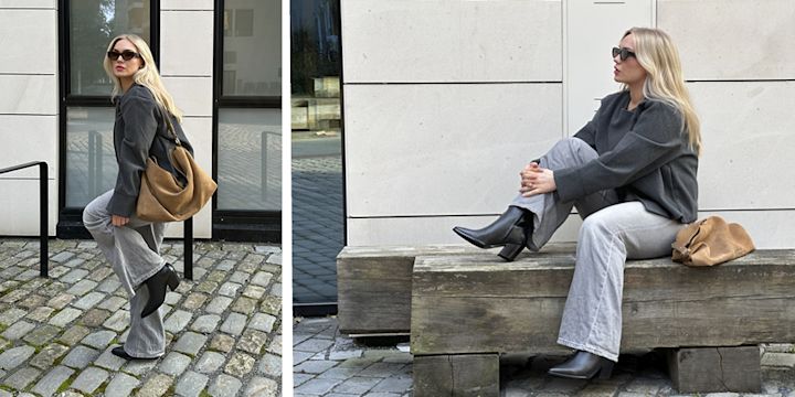 Kvinne med solbriller, grå genser og lyse bukser som poserer stående på brostein og sittende på en trebenk utenfor en bygning med lyse vegger.