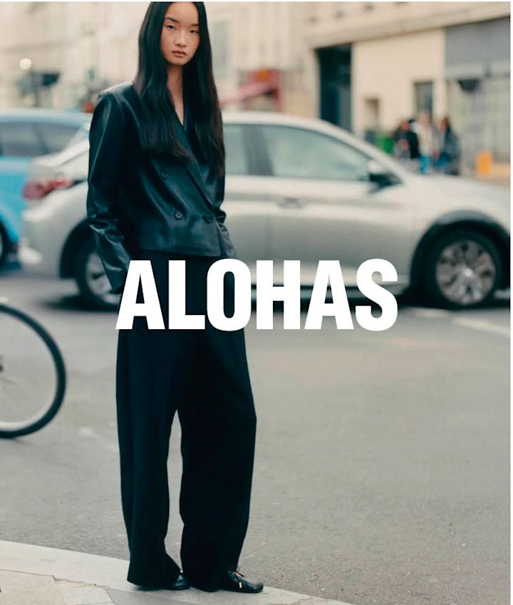 Person i svart antrekk med svarte skinnsko på gaten, med "ALOHAS" tekst over bildet og biler i bakgrunnen.