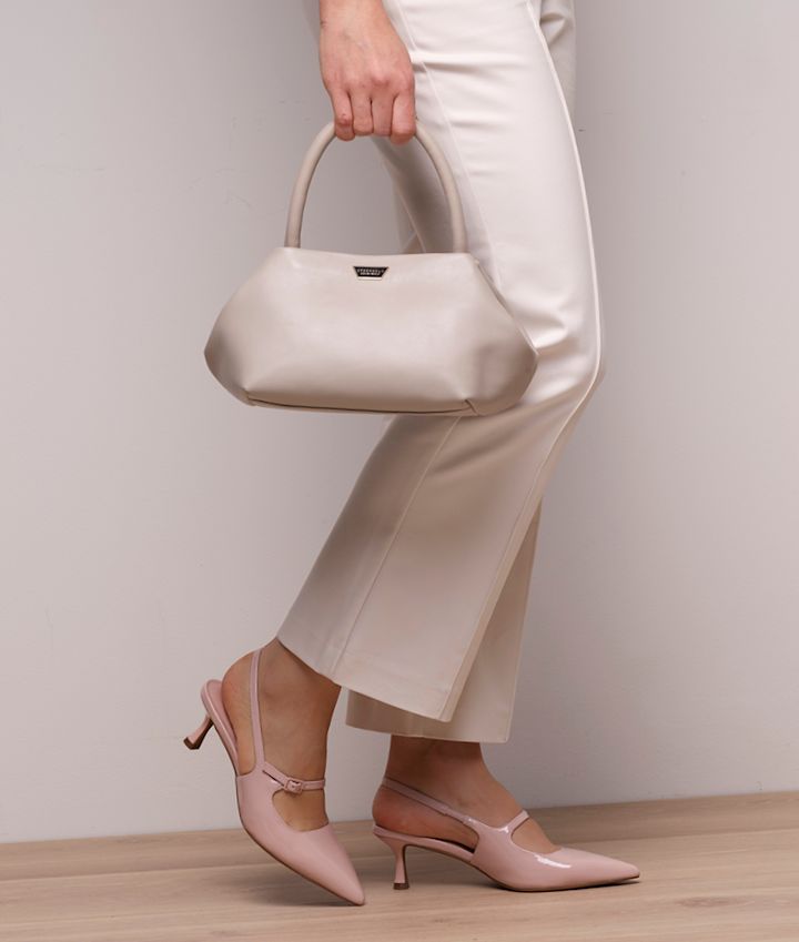 Kvinne i kremhvite bukser med rosa lakk slingback pumps med lav hæl og spiss tå, holder en beige håndveske.