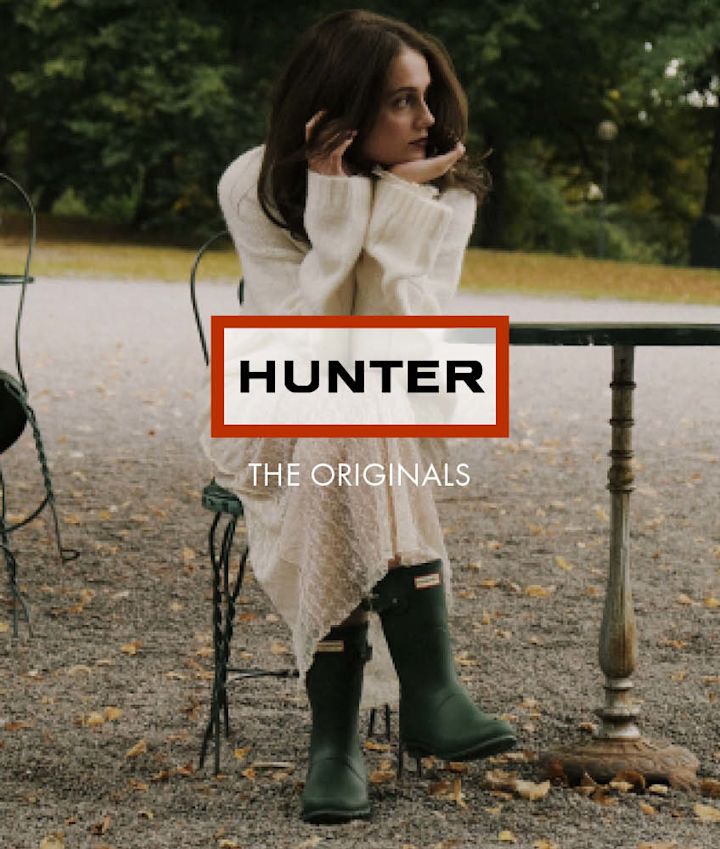 Kvinne sitter utendørs i hvit kjole med mørkegrønne Hunter-gummistøvler i klassisk stil.