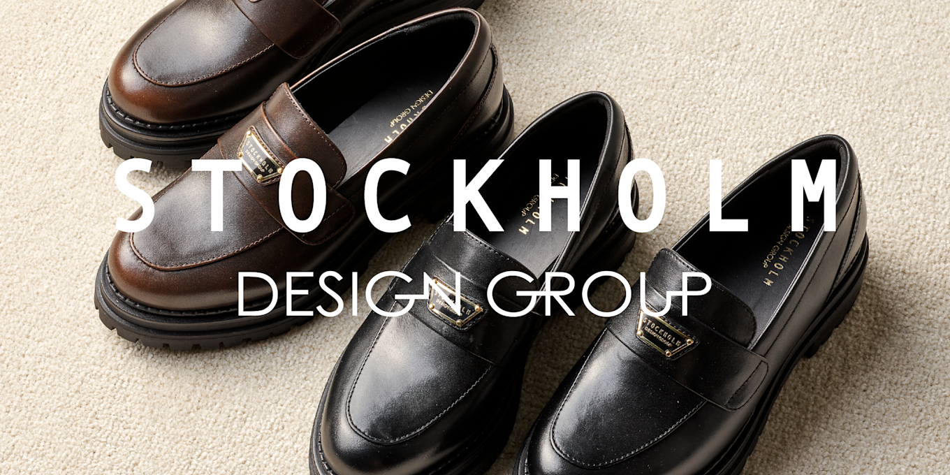 Elegante loafers i brunt og svart skinn fra Stockholm Design Group, plassert på beige underlag med kraftige såler.