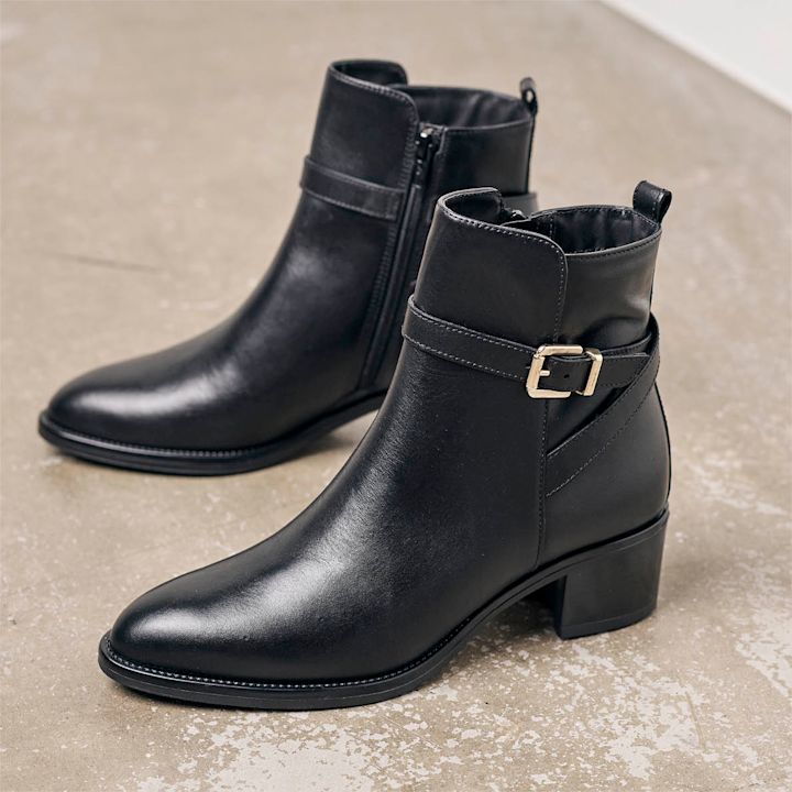 sorte ankelboots med spenne stående på gulv